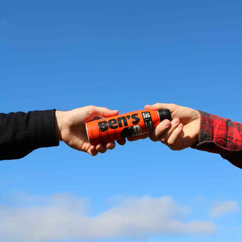Ben's Tick Repellent 6 oz. Eco-Spray handing to friend in front of sky