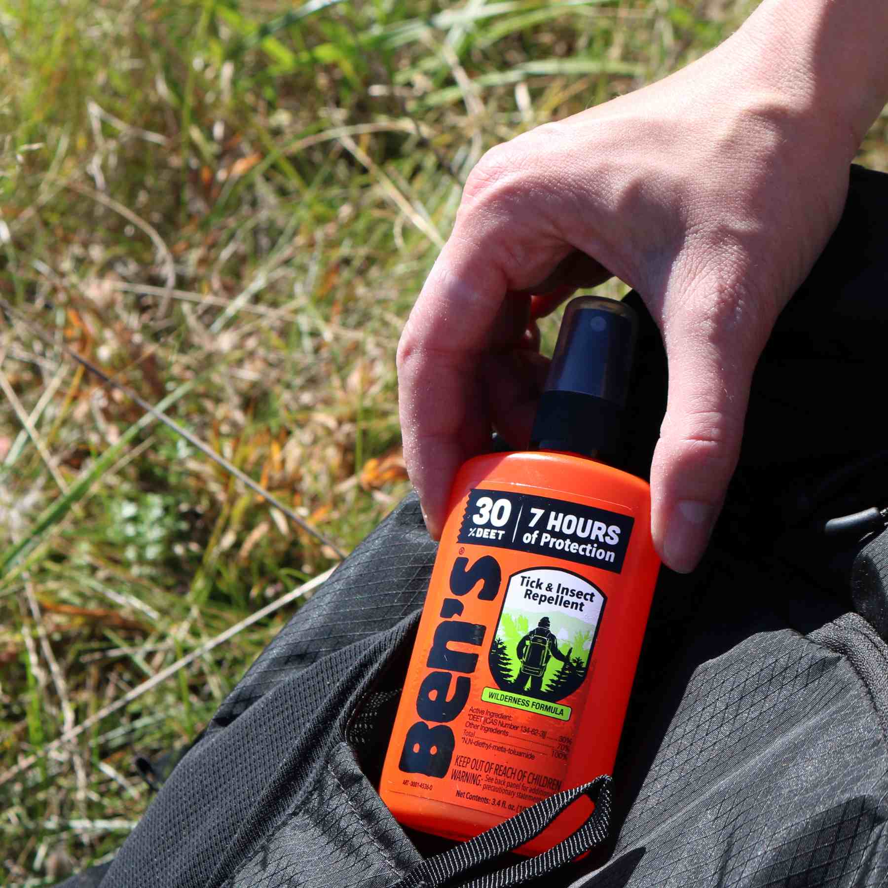 Hand removing Ben's 30 DEET3.4 oz insect repellent from black backpack pocket