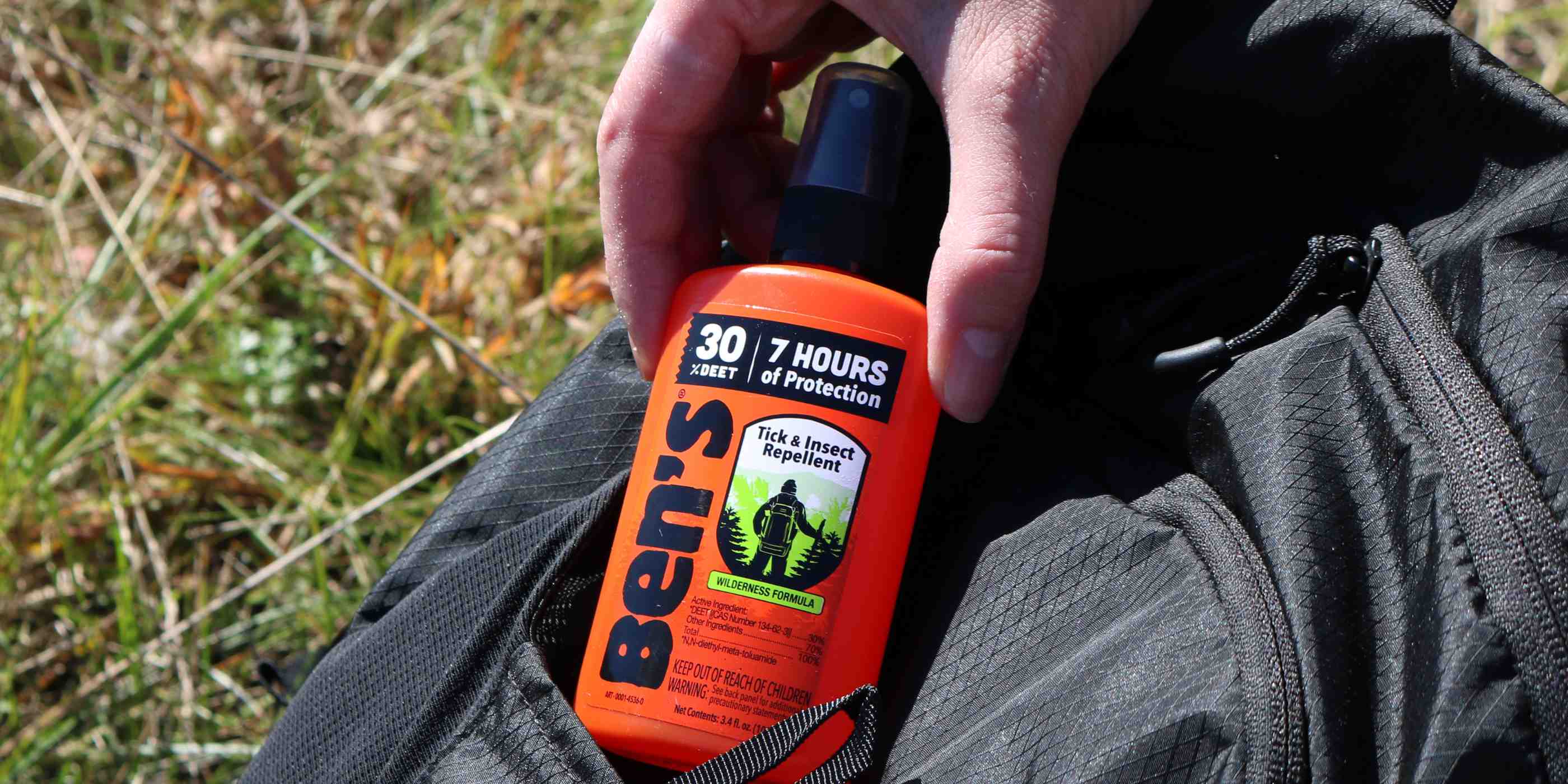 Hand removing Ben's 30 DEET3.4 oz insect repellent from black backpack pocket
