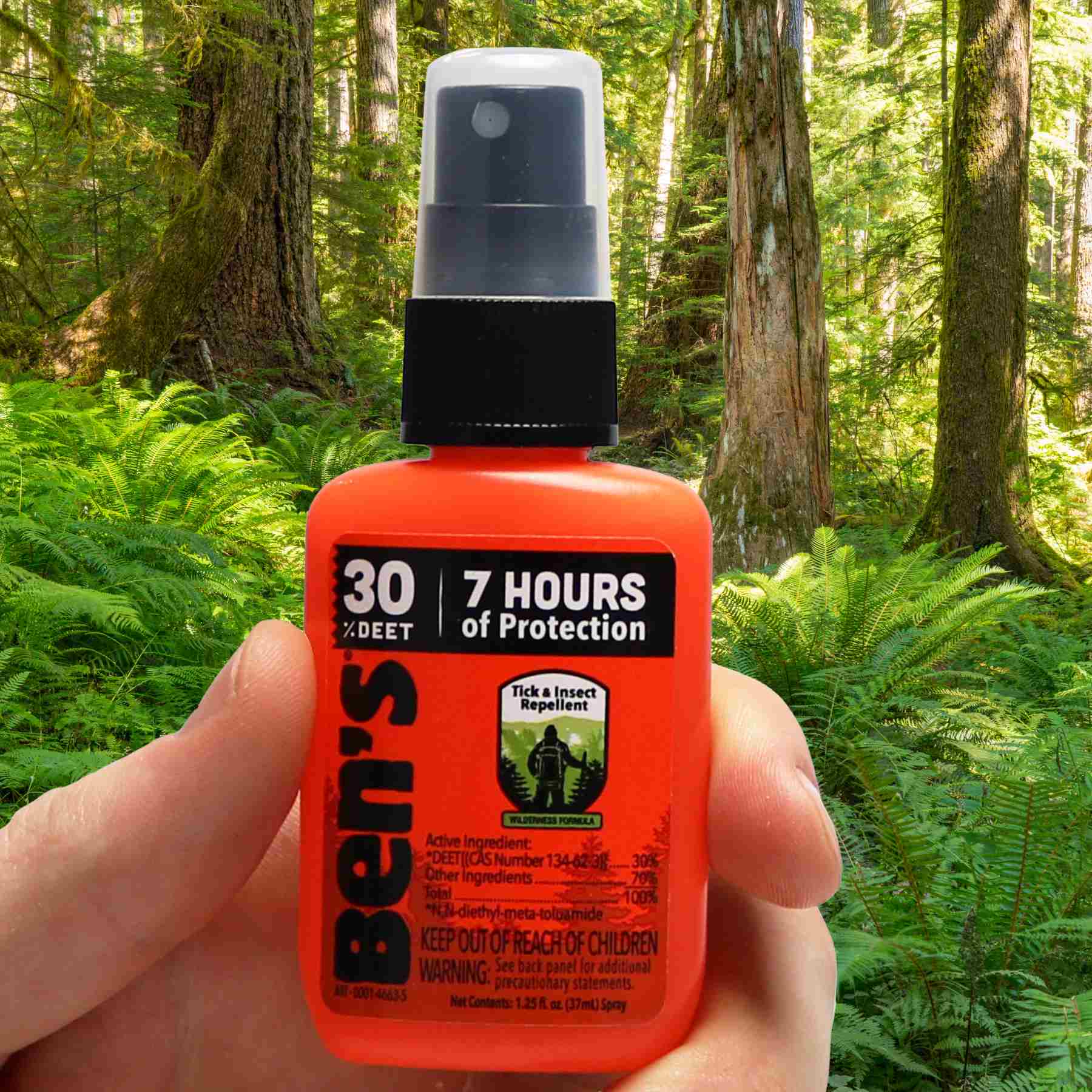 Hand holding Ben's 30 1.25 oz repellent in front of jungle woods