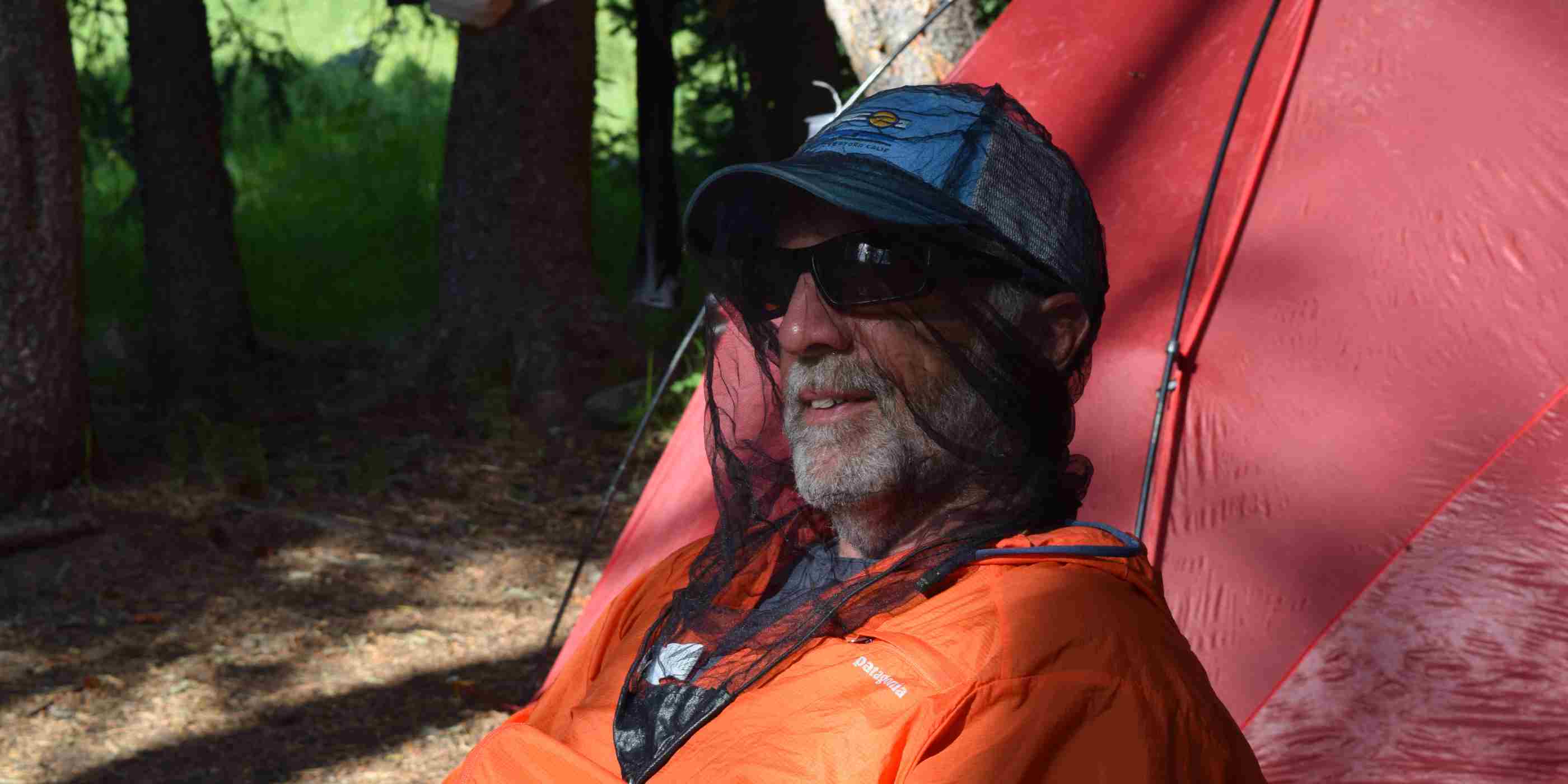 Man wearing Ben's Invisinet Head Net in Orange Jacket in front of red tent in the woods