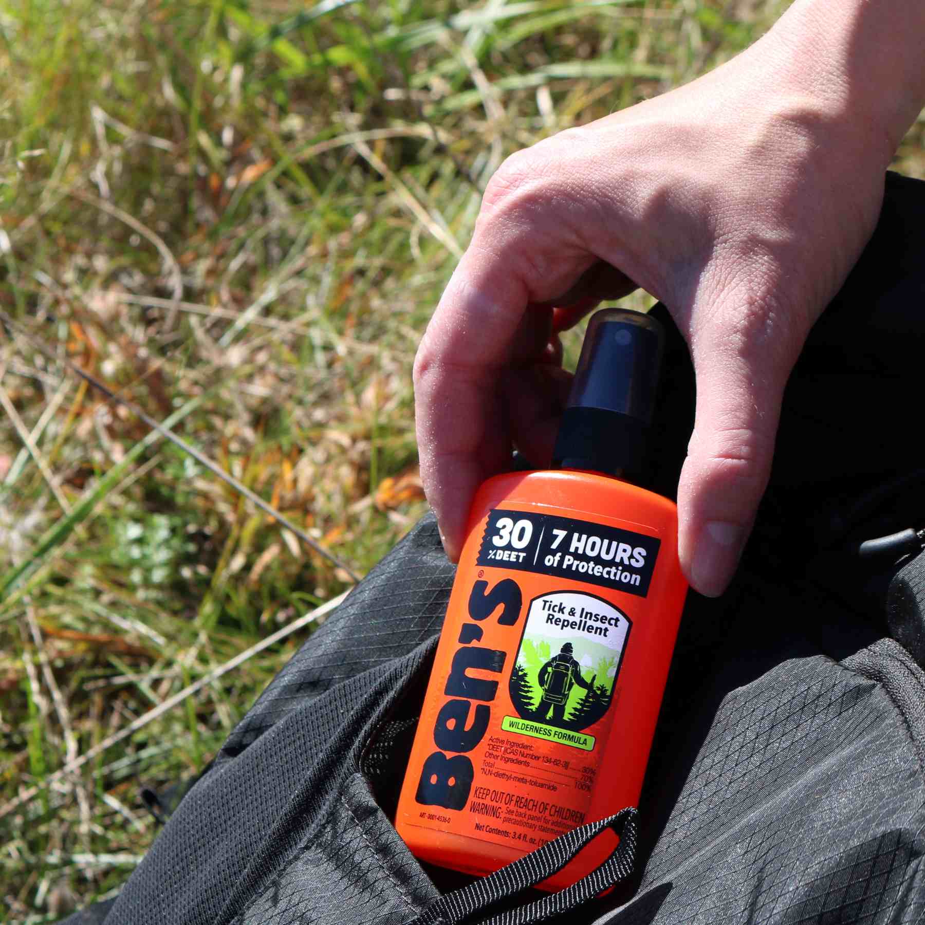 Hand removing Ben's 30 DEET3.4 oz insect repellent from black backpack pocket 