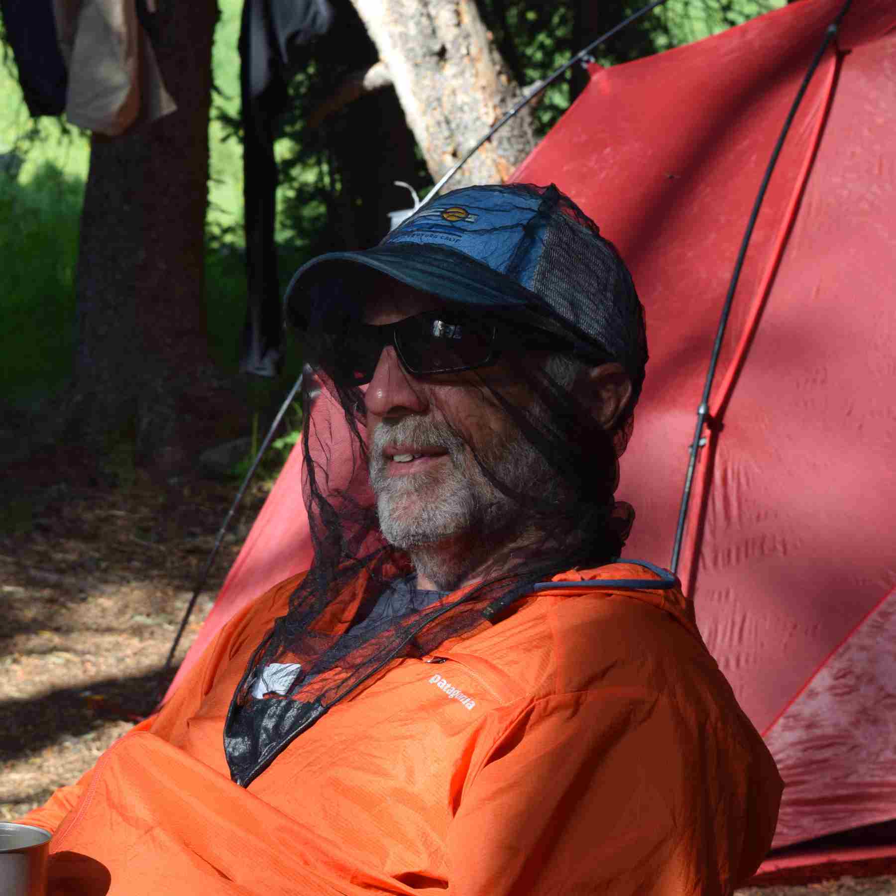 Man wearing Ben's Invisinet Head Net in Orange Jacket in front of red tent in the woods