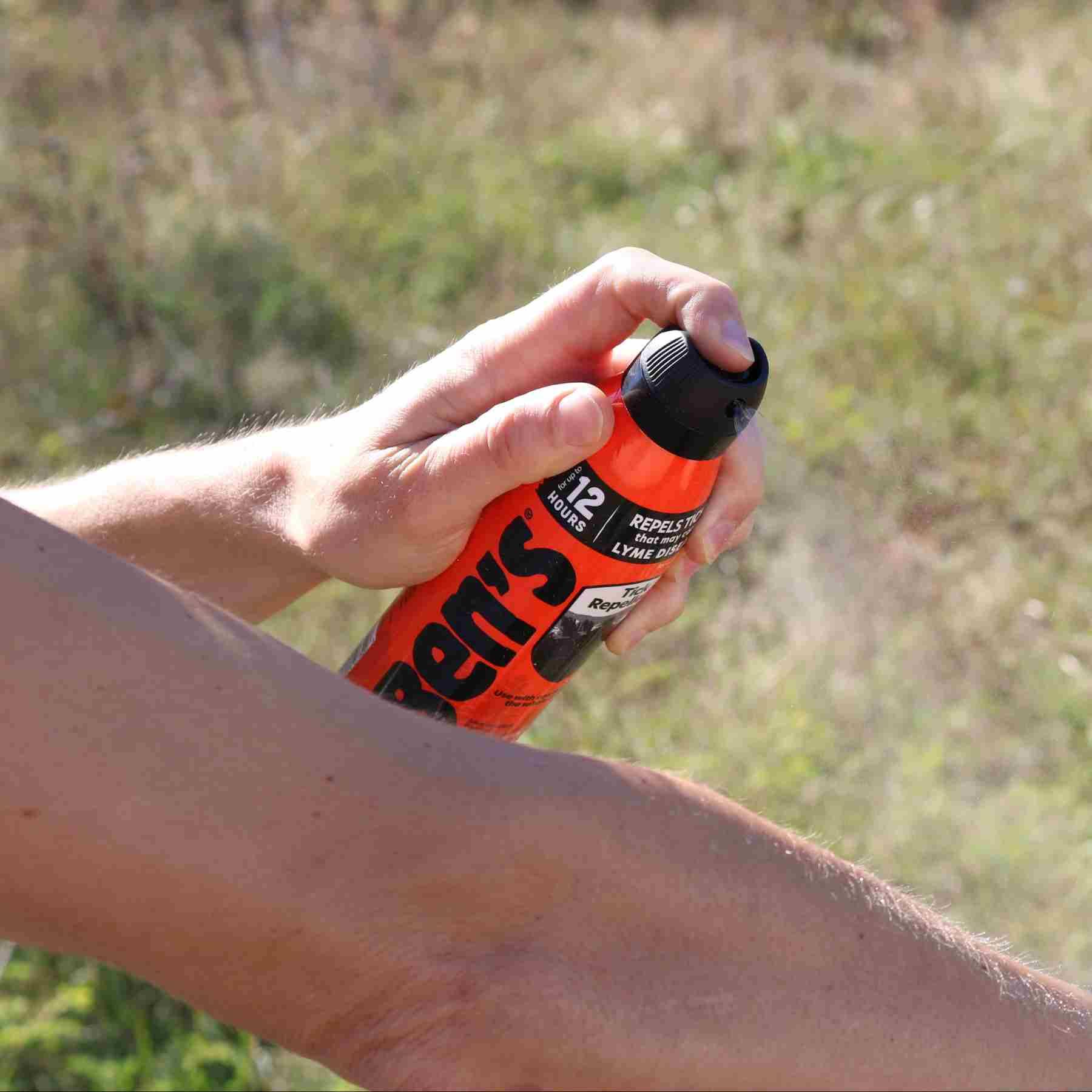 Person spraying Ben's Tick Repellent 6 oz on arm in front of grassy area