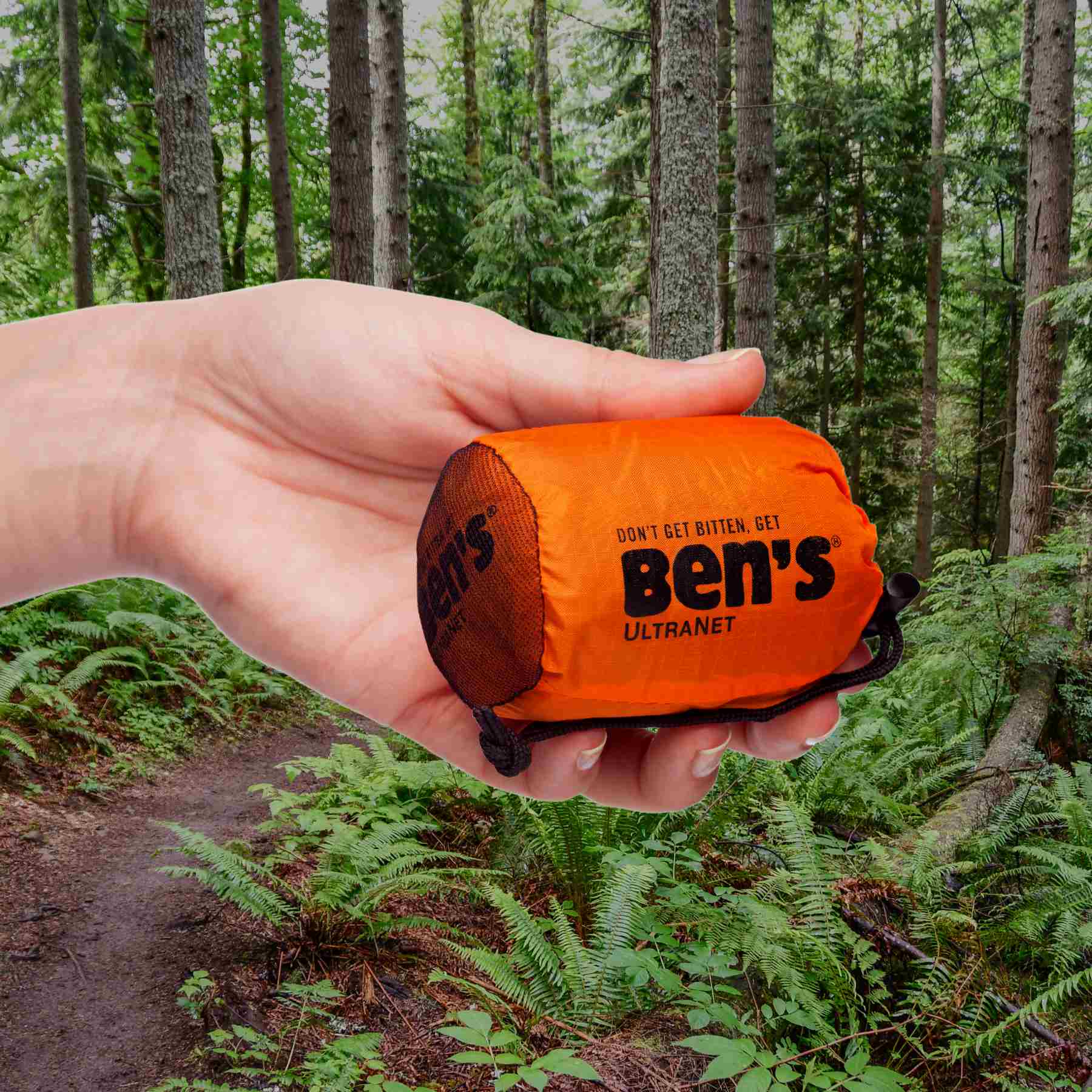 Hand holding Ben's Ultranet Head Net in sleeve in front of jungle woods trail