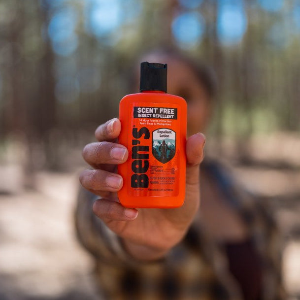 person holding insect repellent lotion bottle in front of face 