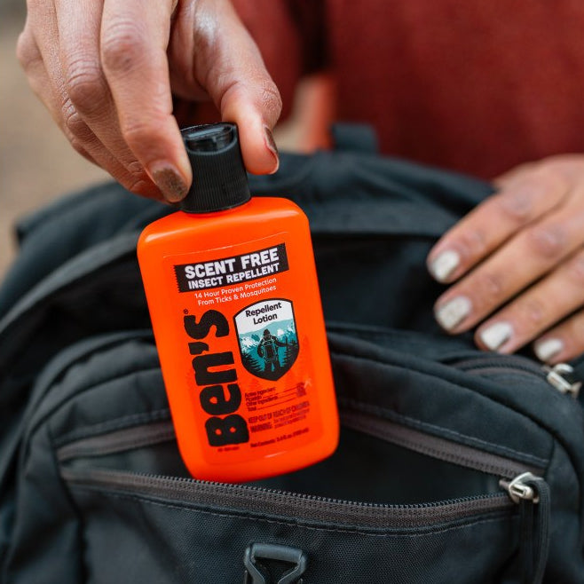 bottle of insect repellent lotion being placed inside of a backpack